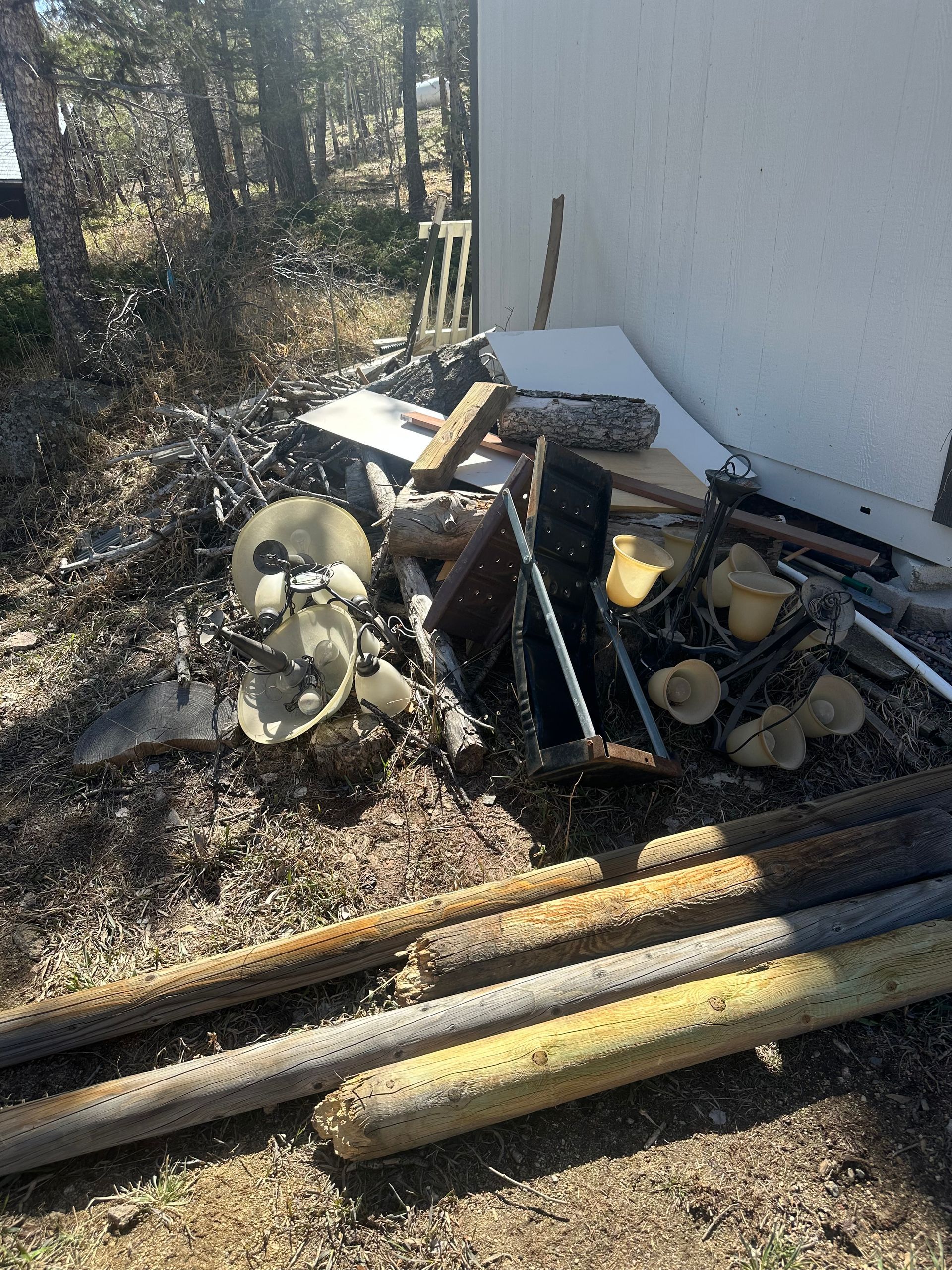Pile of trash and debris next to a building with tree branches and grass in the background in Erie, CO.
