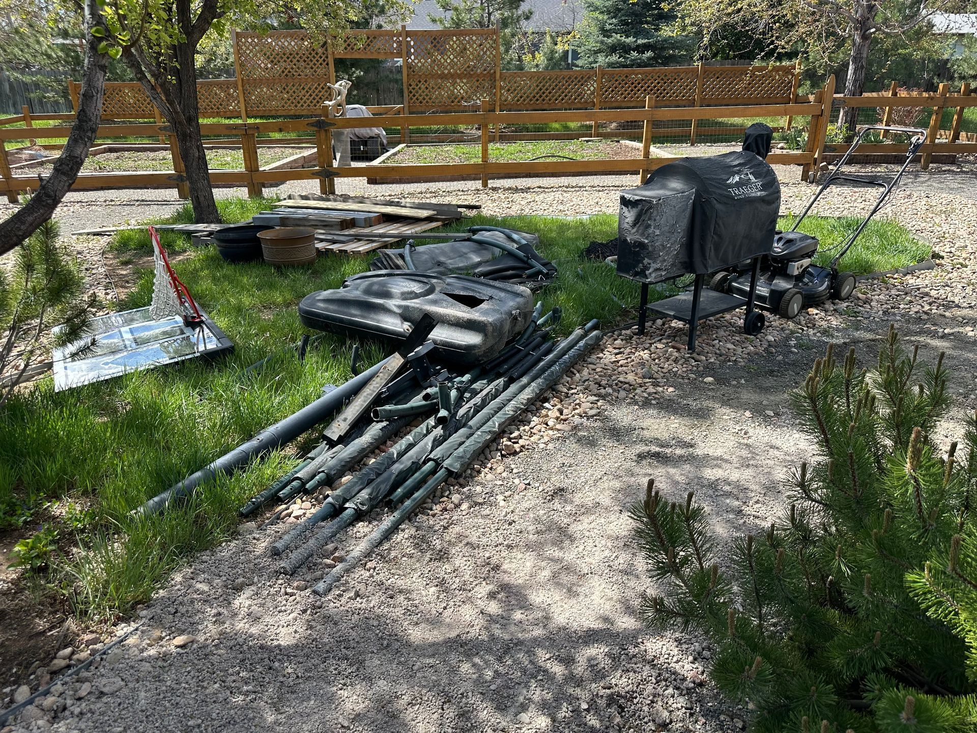 Backyard with scattered disassembled basketball hoop, grill, and debris on gravel and grass.