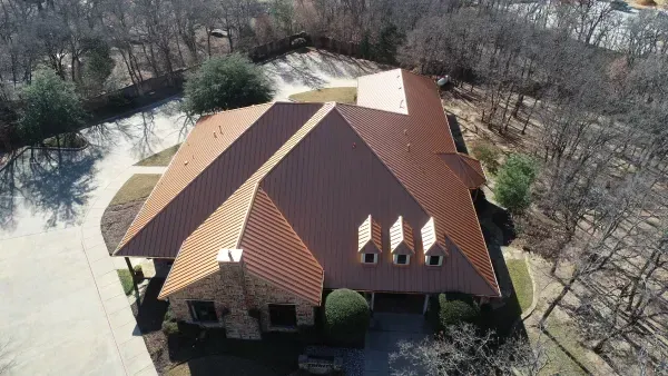 Aerial view of a large house with a brown roof surrounded by trees and flooded yard.