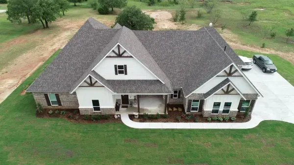 Aerial view of a large gray-roofed house with white trim, surrounded by lawn and trees.