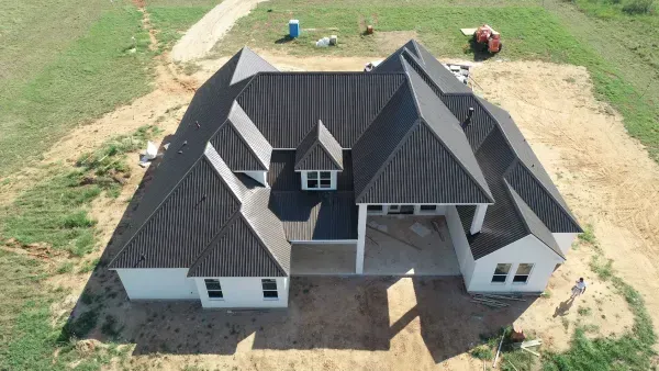 Aerial view of a newly built gray house with a dark roof on a bare lot.