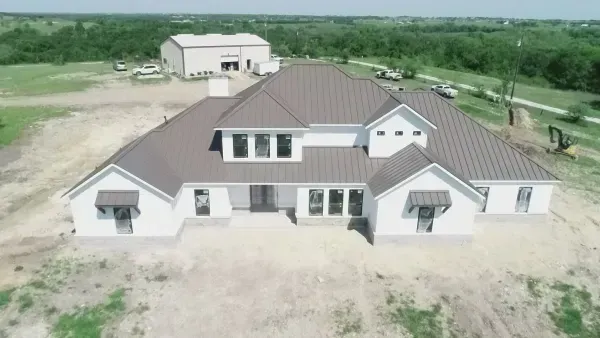 Aerial view of a large white house with a brown roof on a rural property surrounded by open fields.