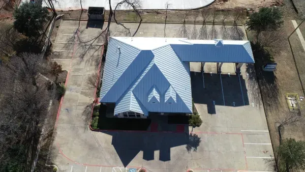 Aerial view of a blue-roofed building with a covered drive-through on a paved lot.
