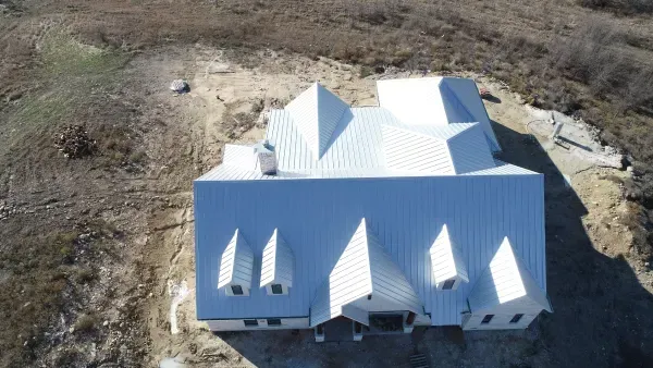 Aerial view of a white metal-roofed house under construction on a cleared lot
