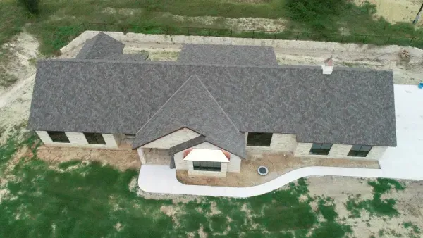 Aerial view of a single-story house with a gray roof and light stone exterior, surrounded by grass.