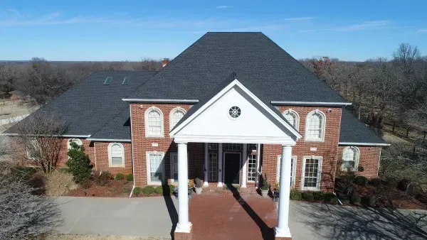 Brick house with white columns and dark roof, viewed from the front under a clear blue sky.