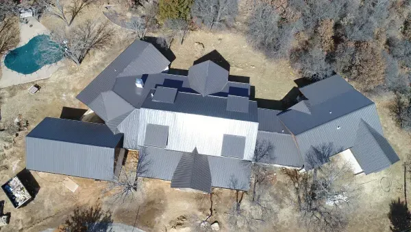 Aerial view of a large gray-roofed house surrounded by leafless trees and a small pool.