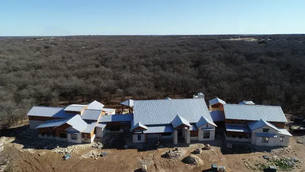 Aerial view of a large metal-roofed building complex surrounded by barren land and dense forest.