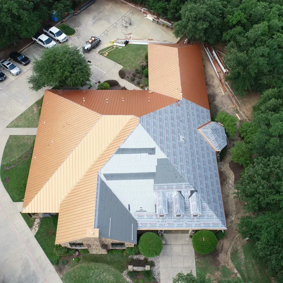 Aerial view of a house with tan and gray roofs surrounded by trees and a driveway.