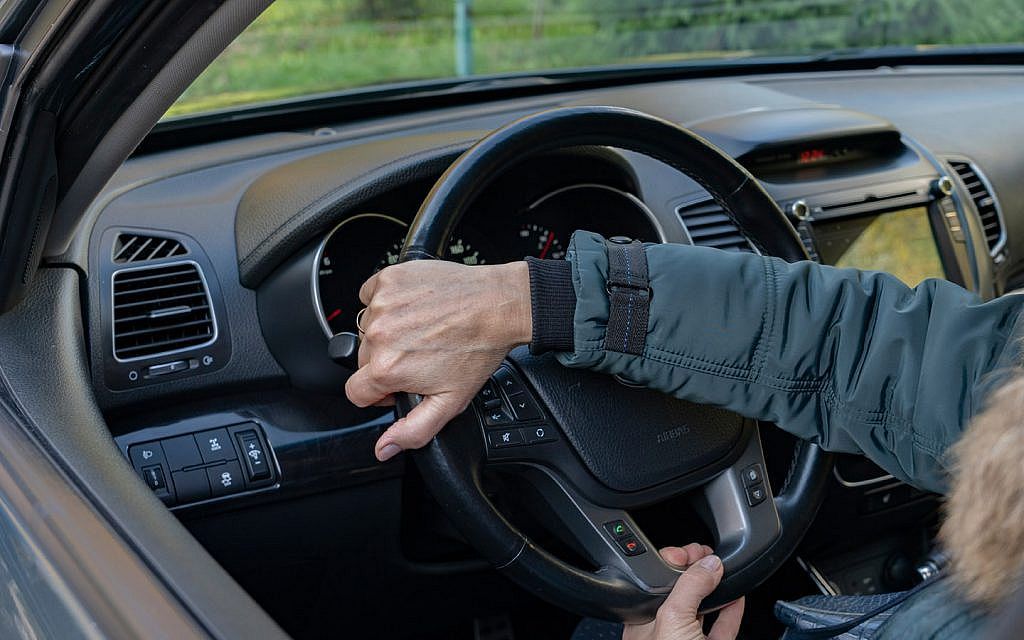 Driver's hands on a black steering wheel inside a car.
