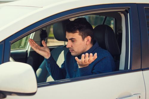 Man in a white car looking frustrated with hands raised, appearing perplexed.