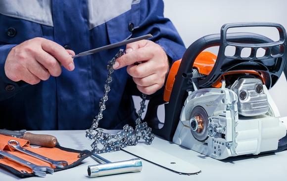 A man is fixing a chainsaw on a table.