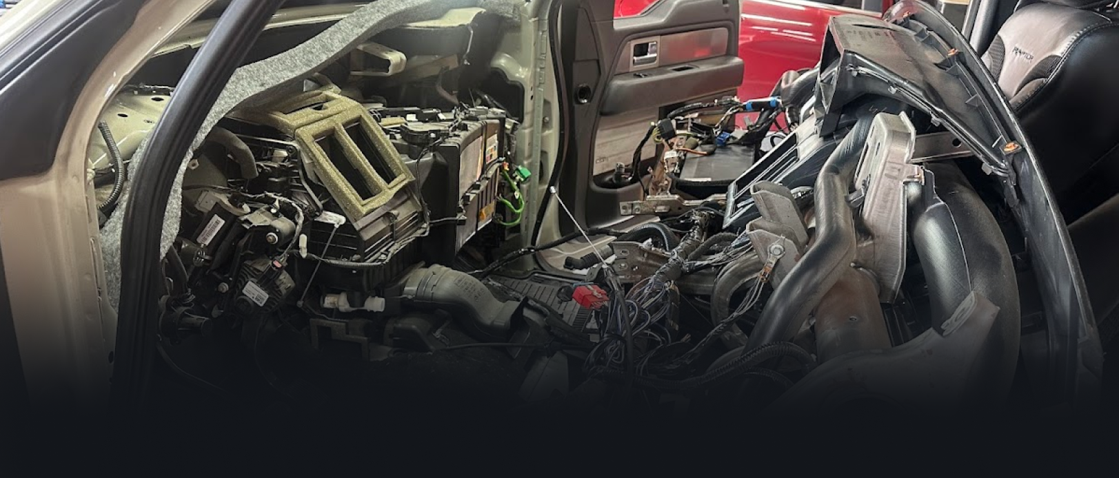 Interior of a vehicle, dashboard removed and components exposed in a workshop.