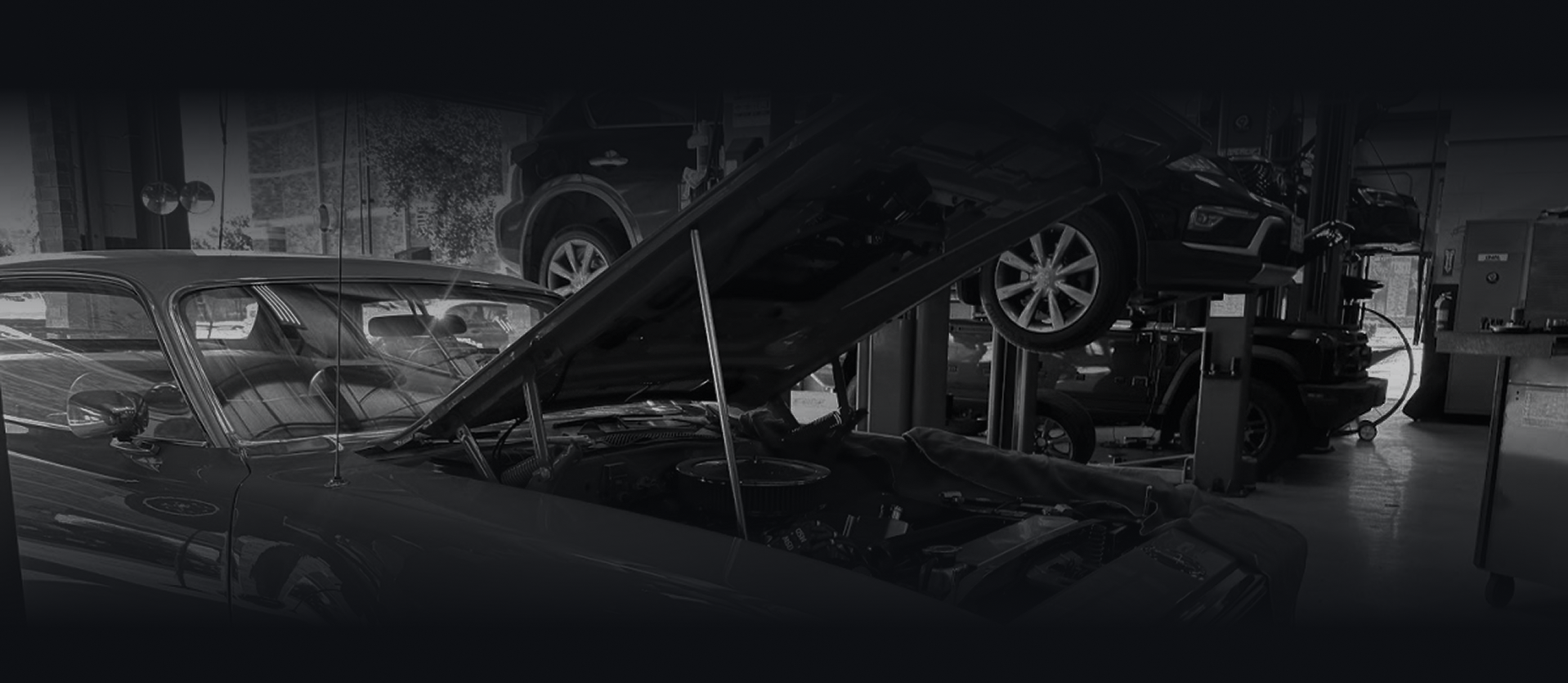Black and white shot of a dark car on a Hunter alignment machine in a garage with the hood open. | Auto Check Sugar Land