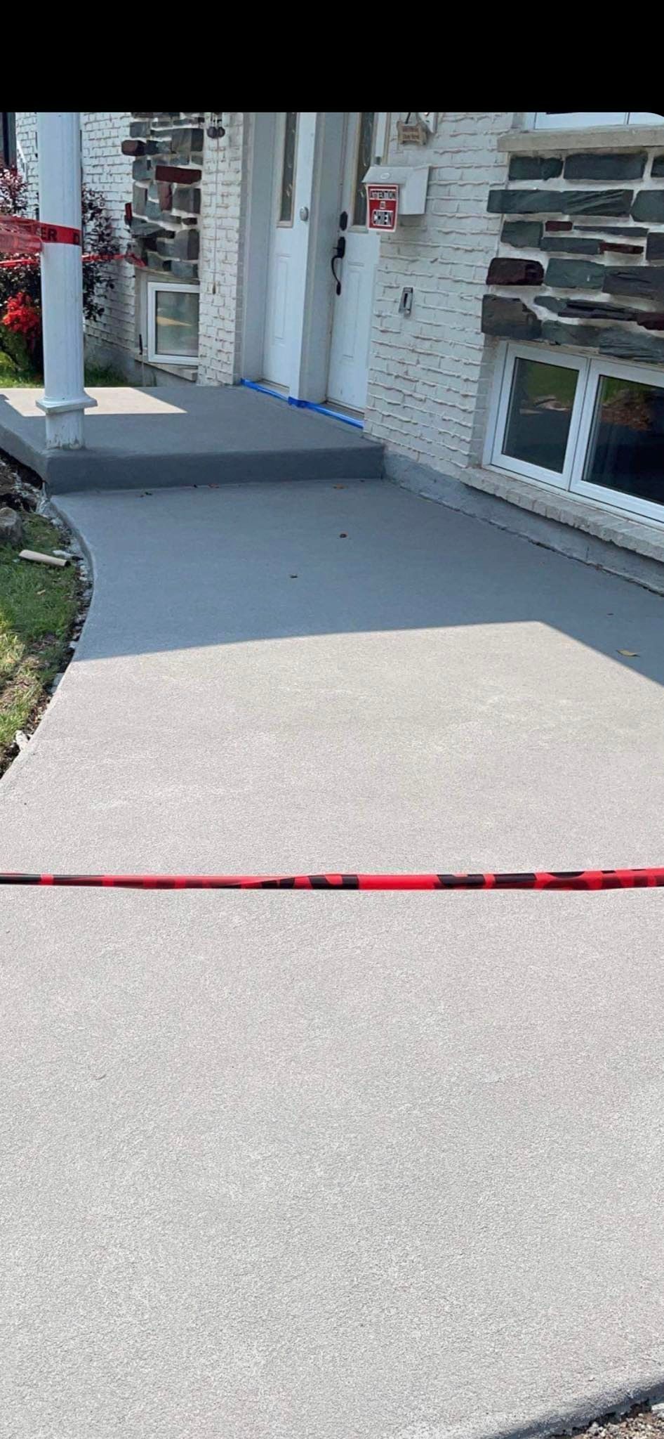 Un trottoir et des marches mènent à une maison. Un ruban rouge et noir est tendu en travers du trottoir.