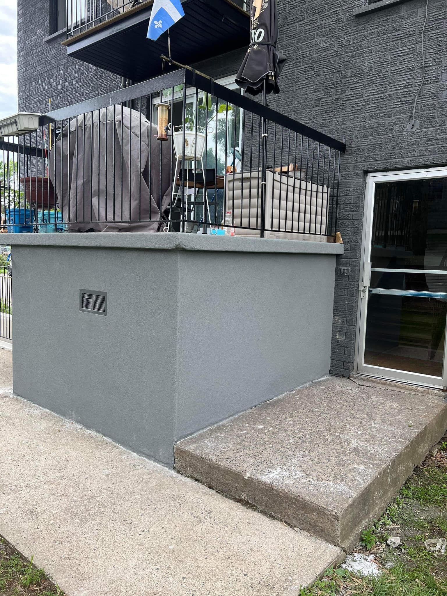 Entrée d'un bâtiment en béton gris avec une petite marche et une rambarde métallique.