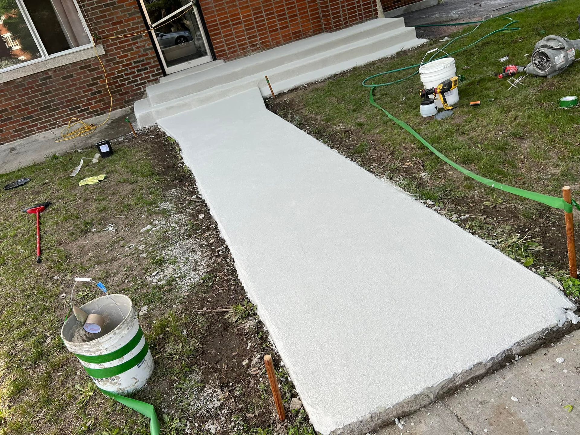 Allée en béton fraîchement coulée menant à l'entrée d'un bâtiment en briques. Entourée de pelouse verte.