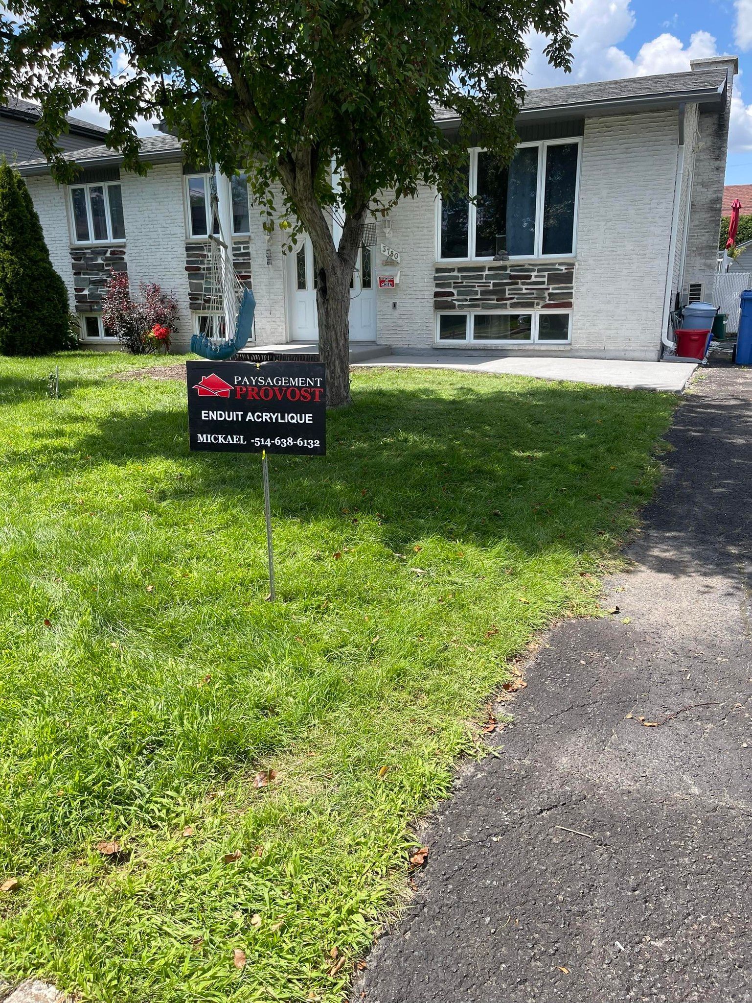 Maison avec panneau sur pelouse verte, arbre devant, journée ensoleillée.