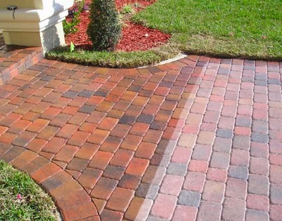 Allée pavée de briques carrées rouges et brunes, bordant une pelouse et un parterre de fleurs.