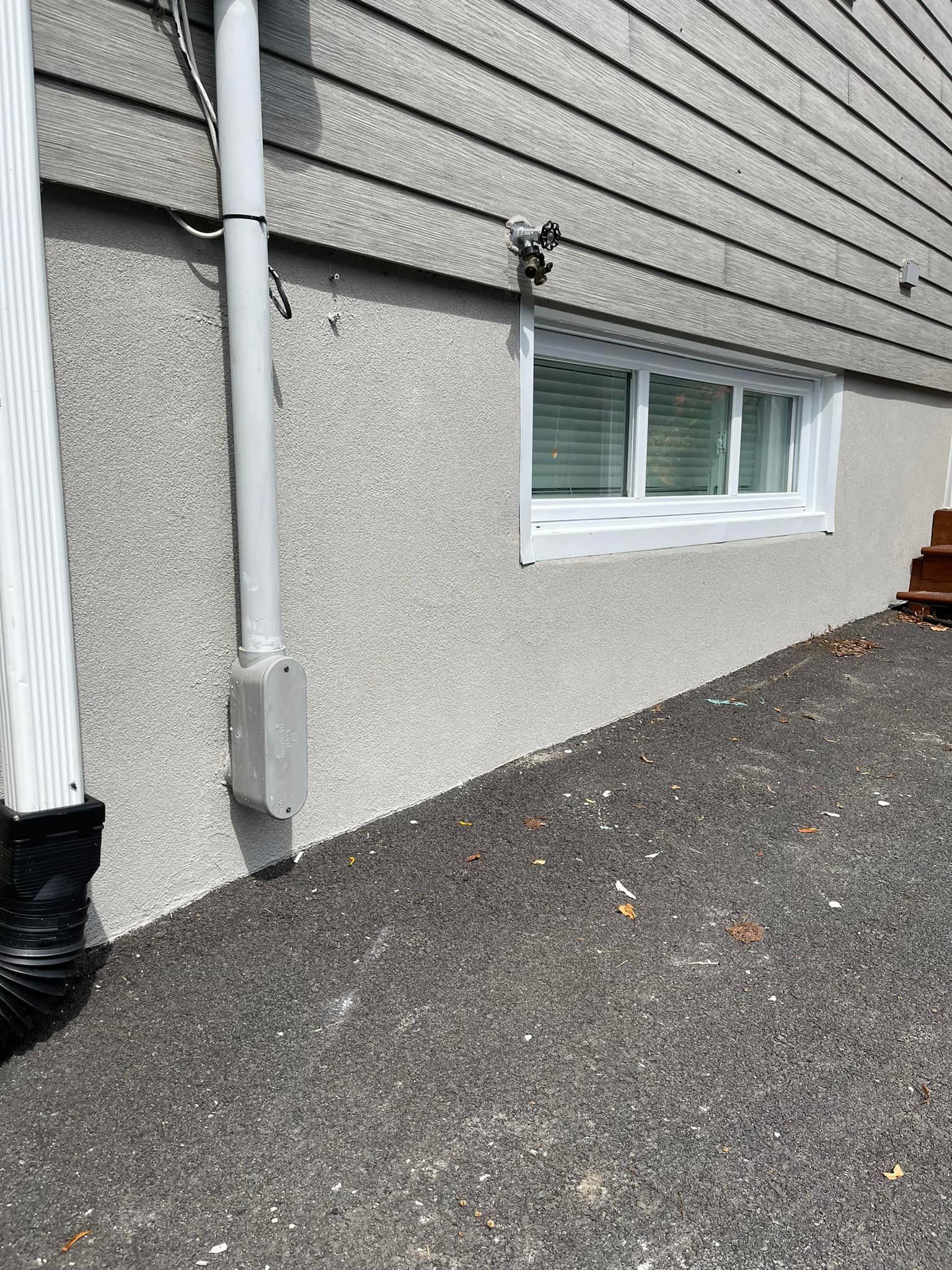 Extérieur d'une maison avec bardage gris, fenêtre, descente de gouttière et sol en gravier.
