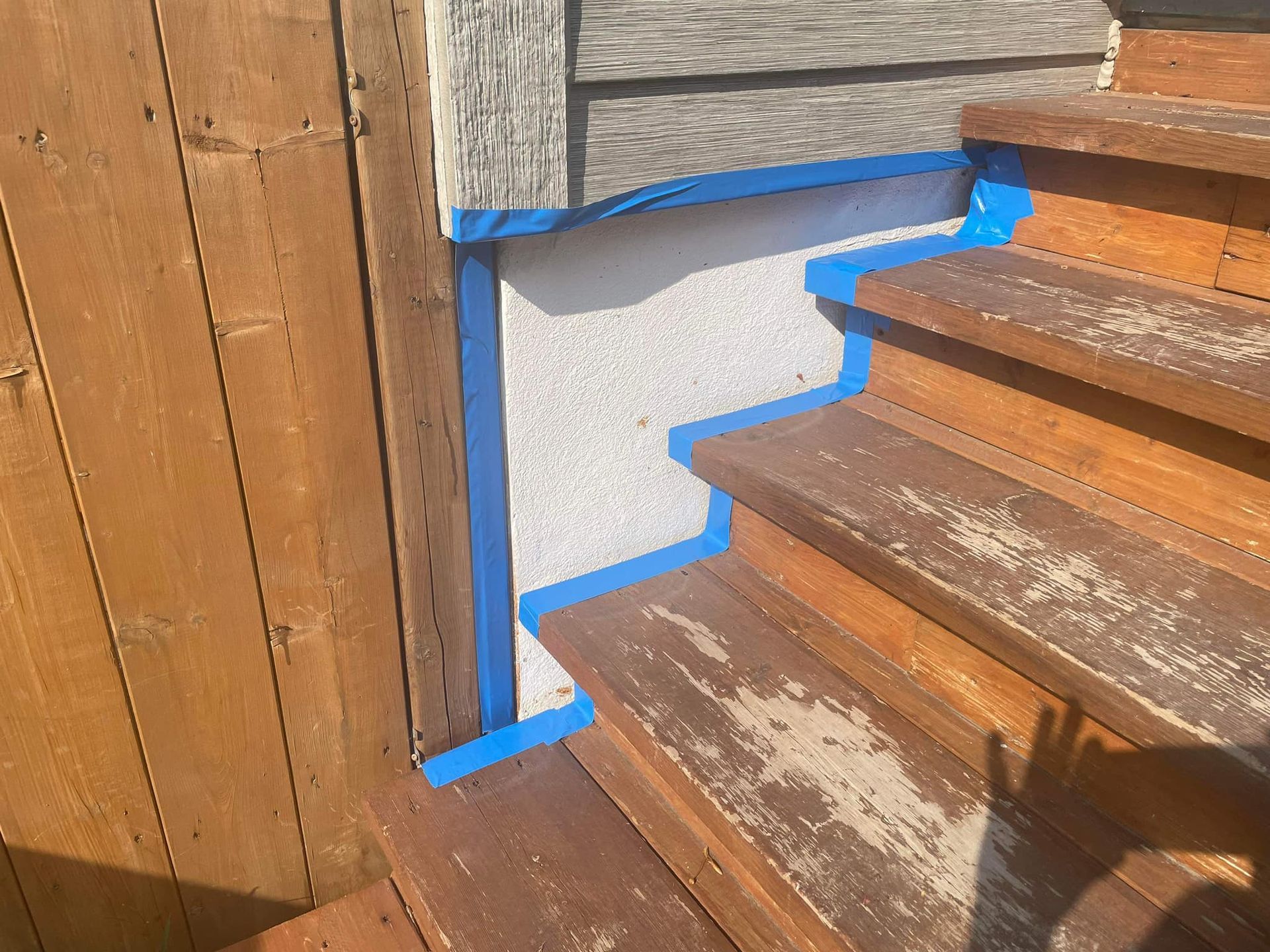 Marches en bois avec ruban adhésif bleu de protection le long du mur, prêtes pour un projet de peinture.