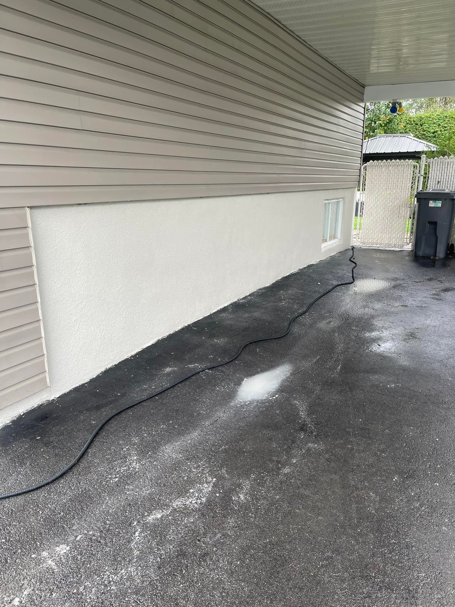Mur extérieur d'un bâtiment avec un bardage brun clair au-dessus d'un enduit texturé, sol en asphalte noir.