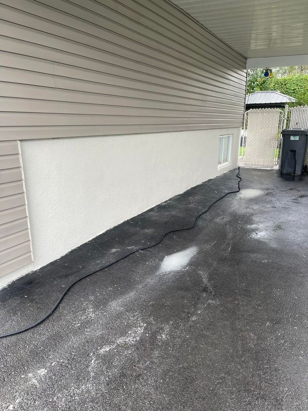 Mur extérieur d'un bâtiment avec un bardage brun clair au-dessus d'un enduit texturé, sol en asphalte noir.