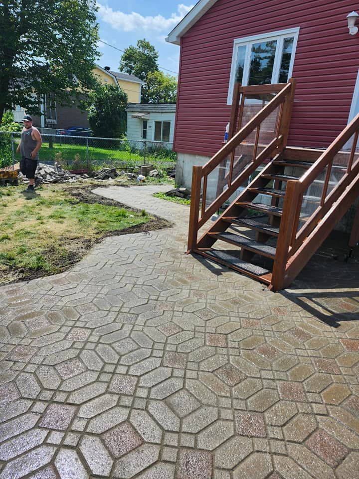 Terrasse en briques et escalier en bois menant à une maison rouge ; une personne se tient sur la pelouse.