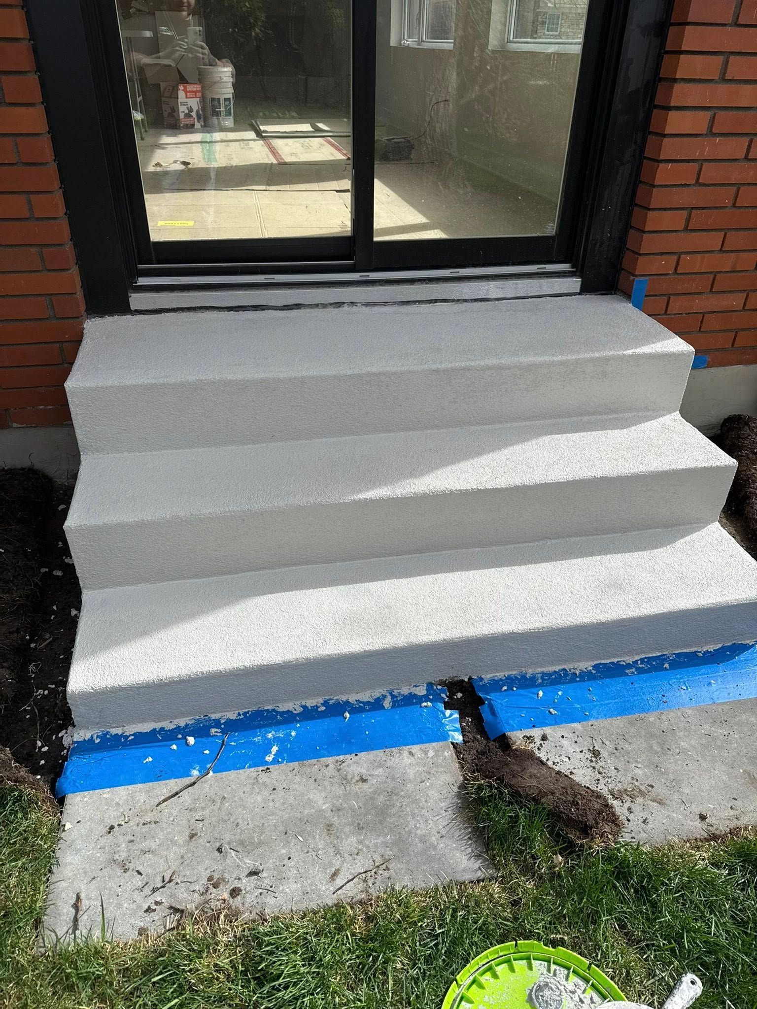 Trois marches en béton gris, nouvellement construites, mènent à une porte coulissante en verre.