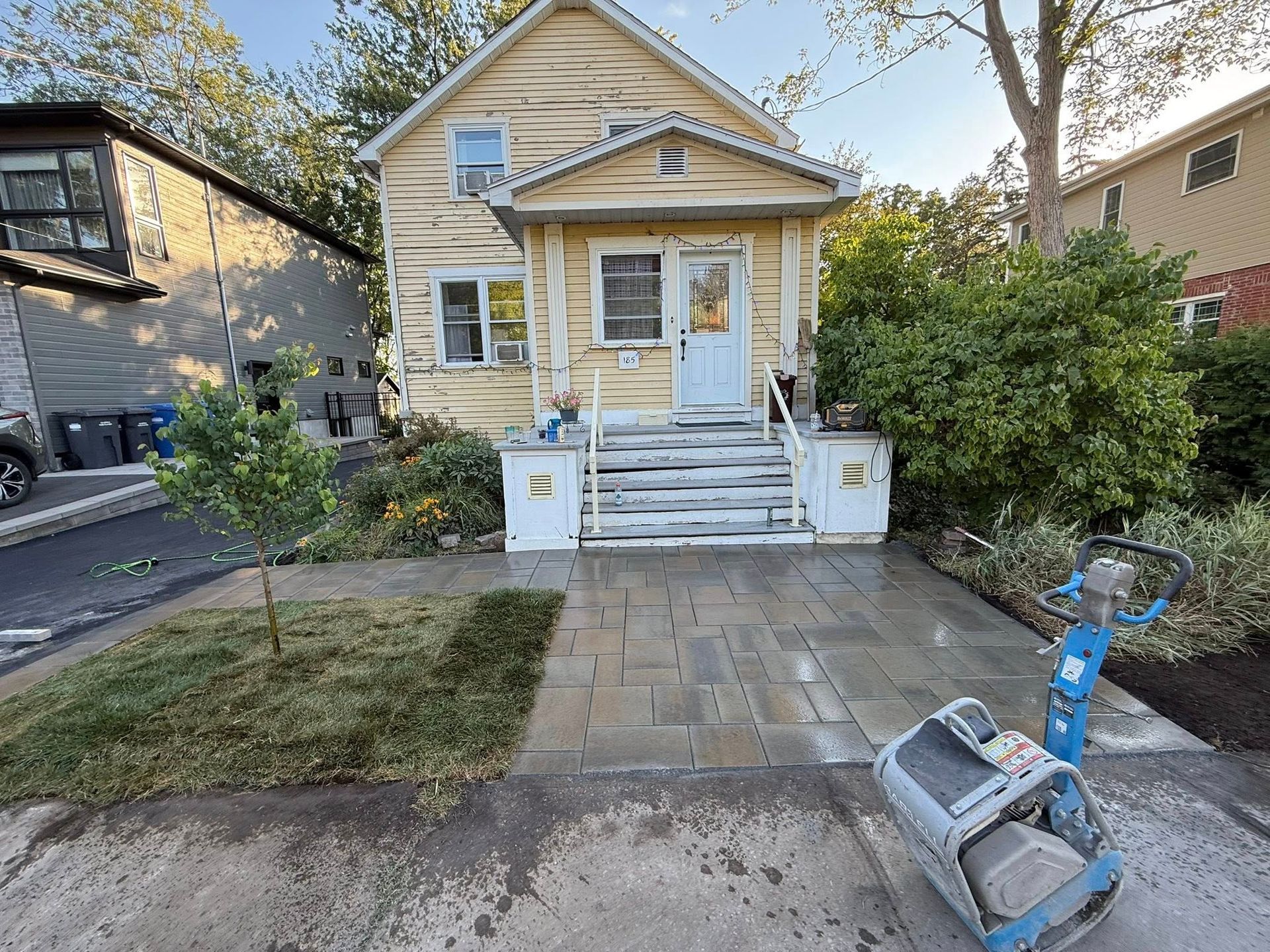 Maison jaune avec une nouvelle allée en pierre ; une machine de jardinage est présente.