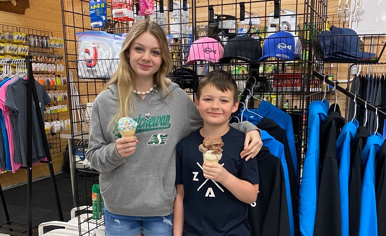 A girl and a boy are standing next to each other in a store holding ice cream cones.