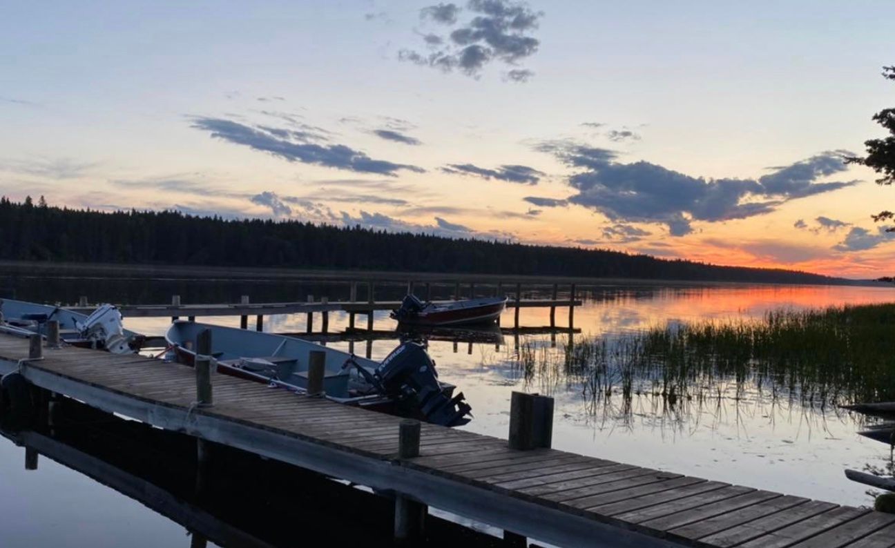 A boat is docked at a dock on a lake at sunset.