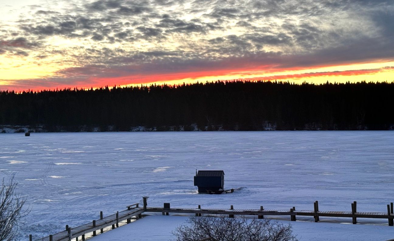 A sunset over a snowy lake with a fence in the foreground