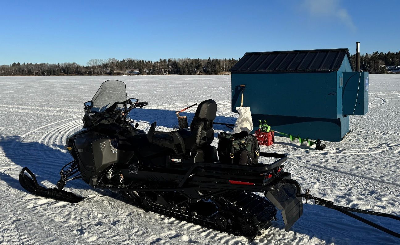 A snowmobile is parked in the snow next to a blue shed.