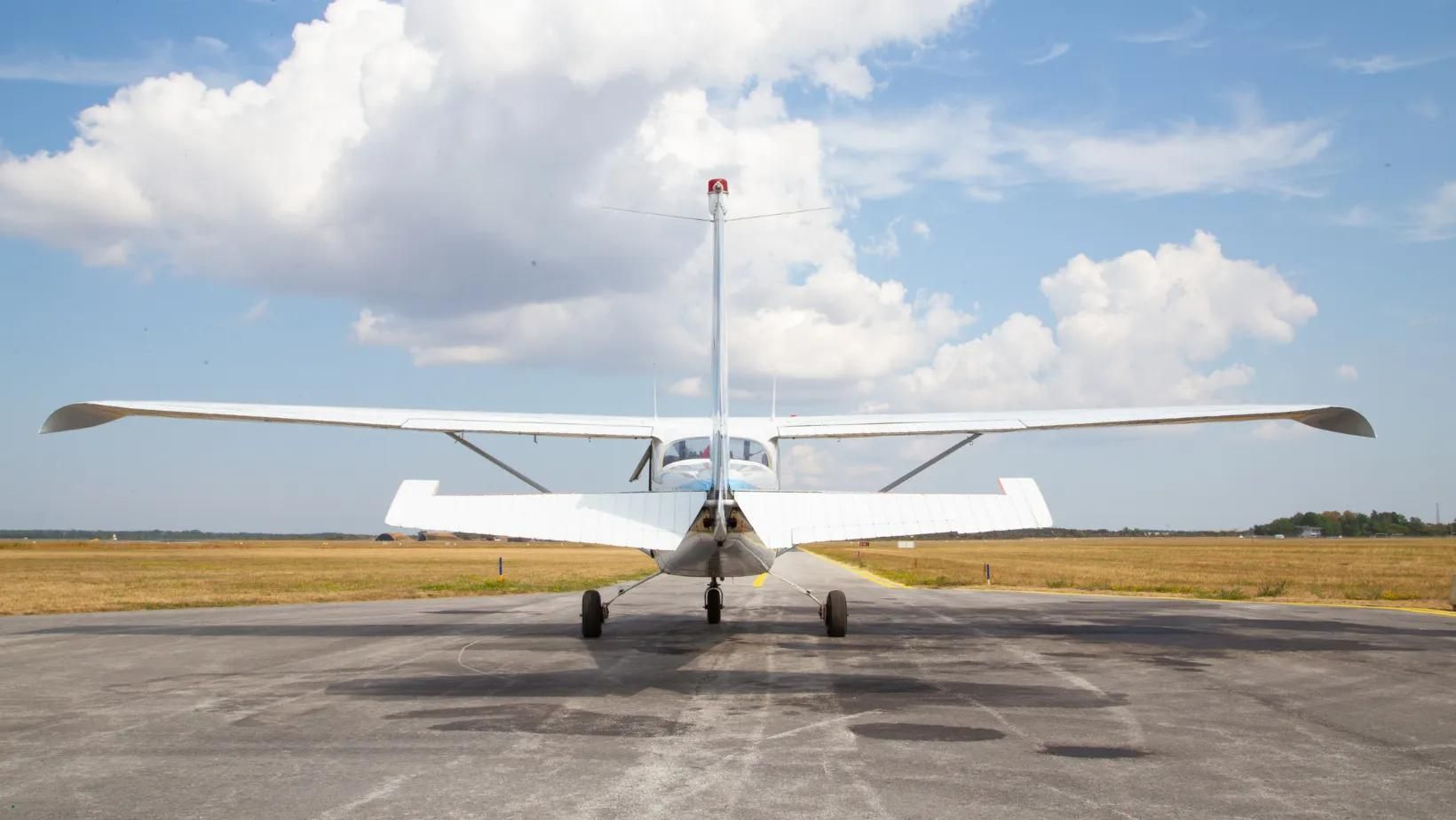 White airplane on a runway, facing camera, wings spread, tail up, blue sky and clouds in background.