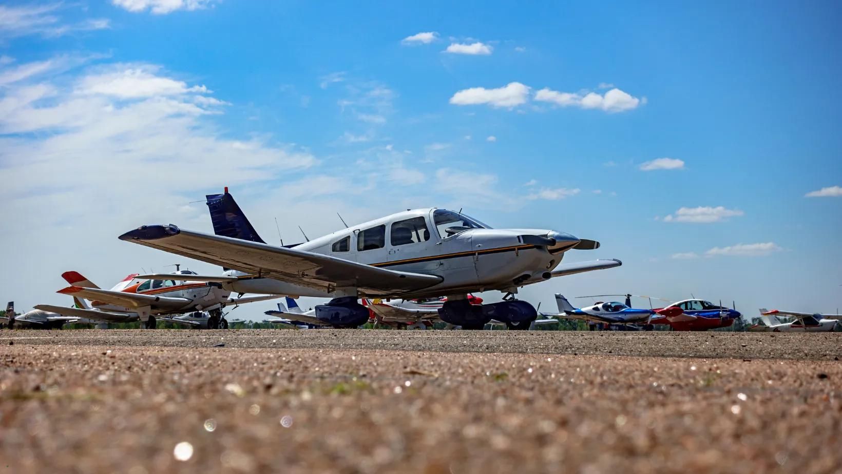 Small airplane on a tarmac with other aircraft under a blue sky.