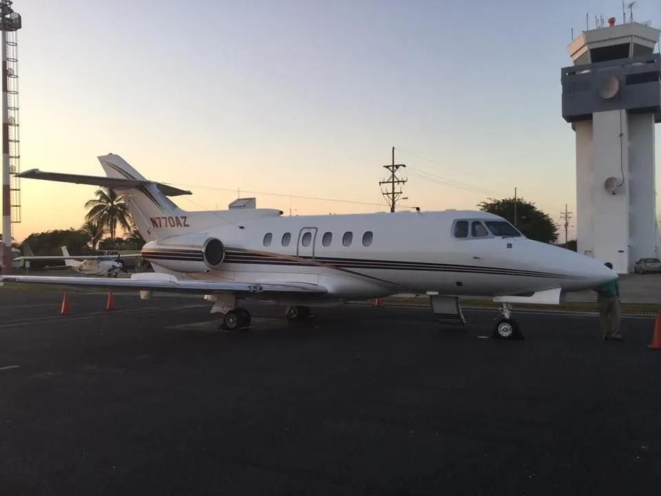 White private jet parked on tarmac next to a control tower.
