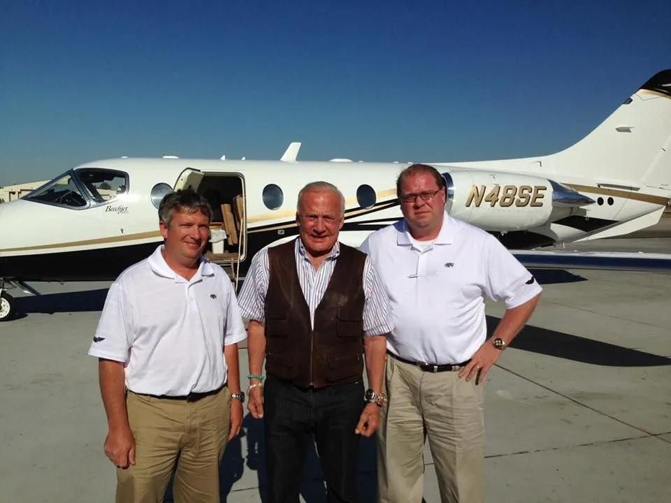 Three men stand in front of a small airplane on a tarmac.