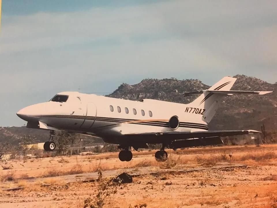 Jet airplane, N770AZ, lands on a dry dirt runway with a mountain backdrop.