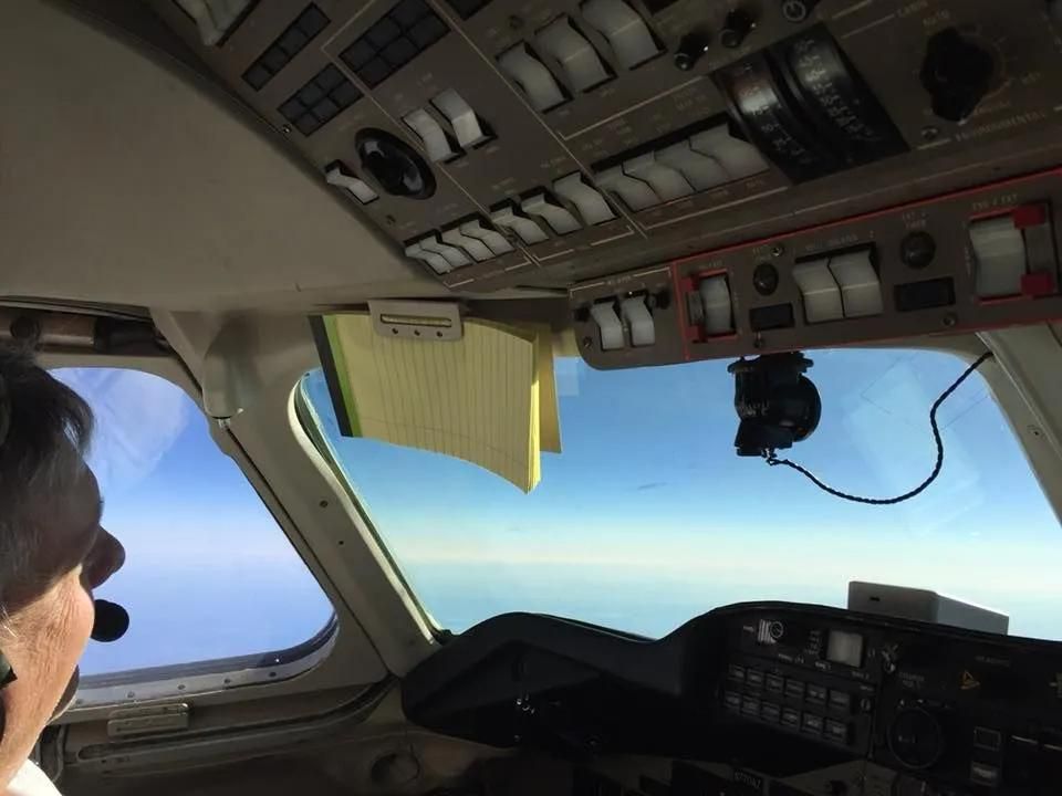 Pilot in cockpit, looking out the window at the sky.