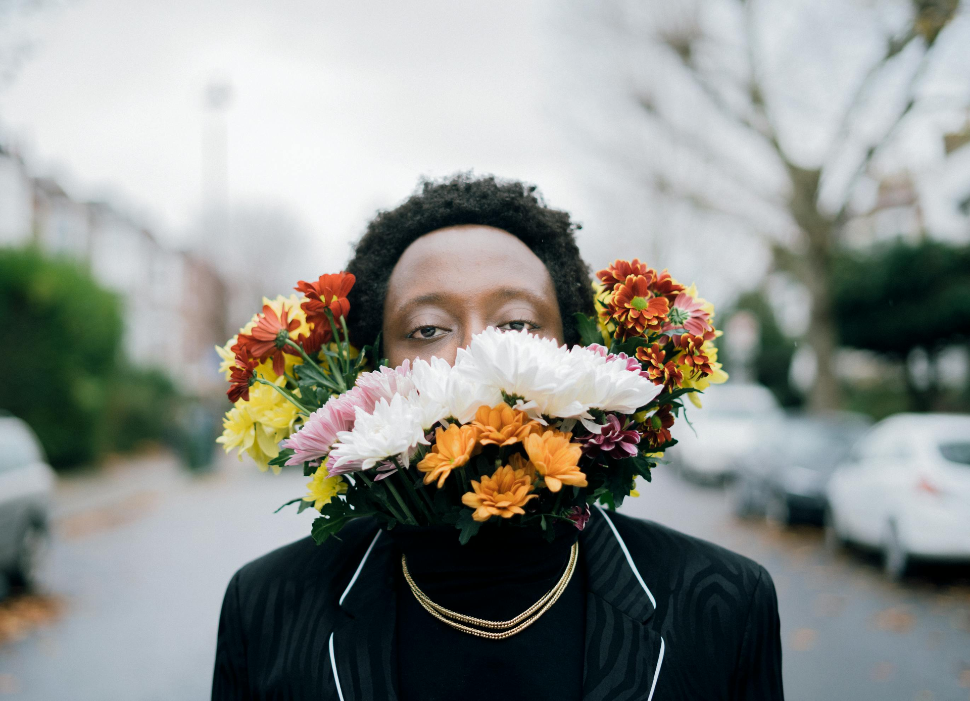 Person with a flower bouquet obscuring their mouth, standing on a residential street.