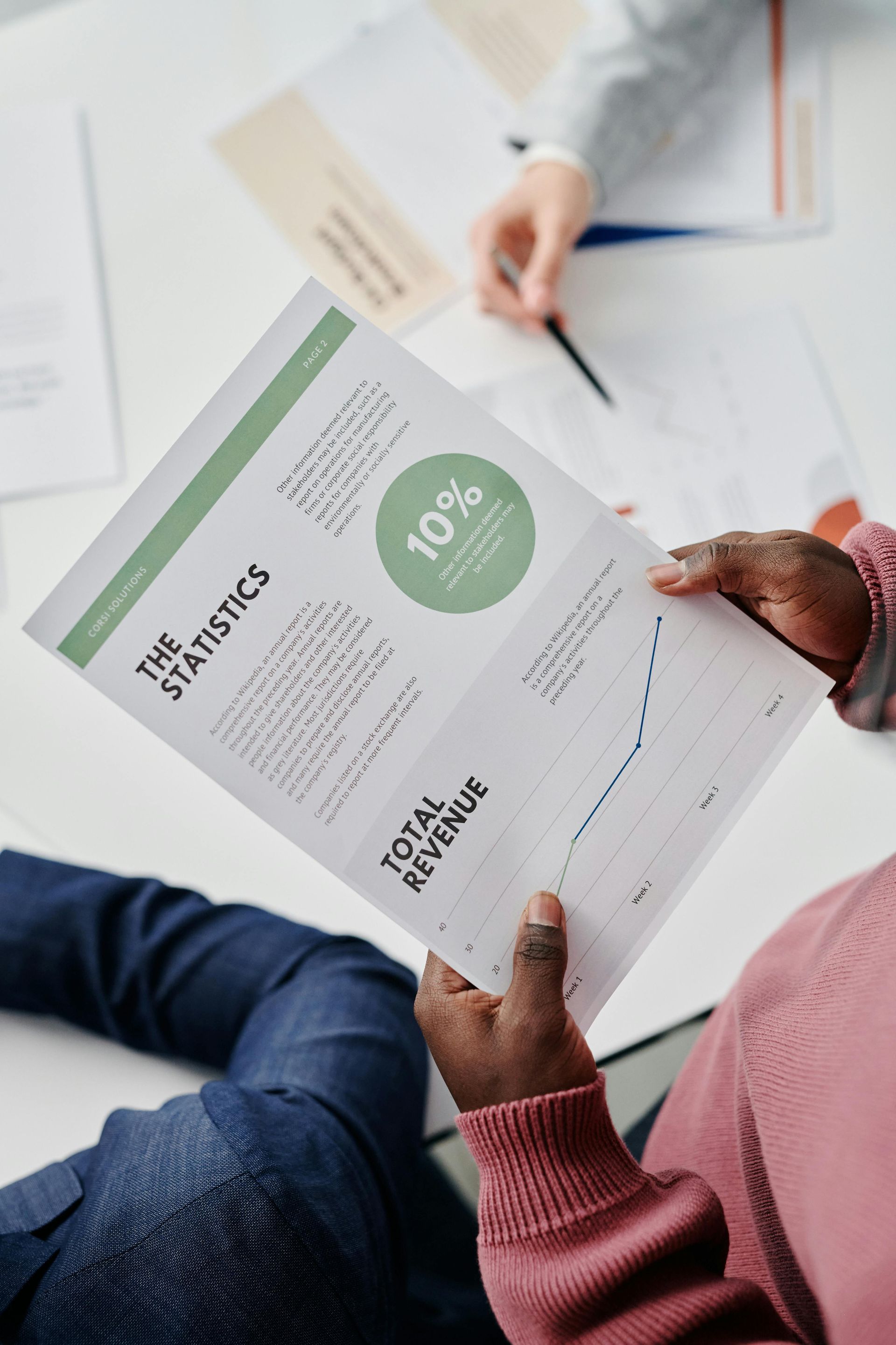 Three people seated at a wooden table in an office, discussing documents.