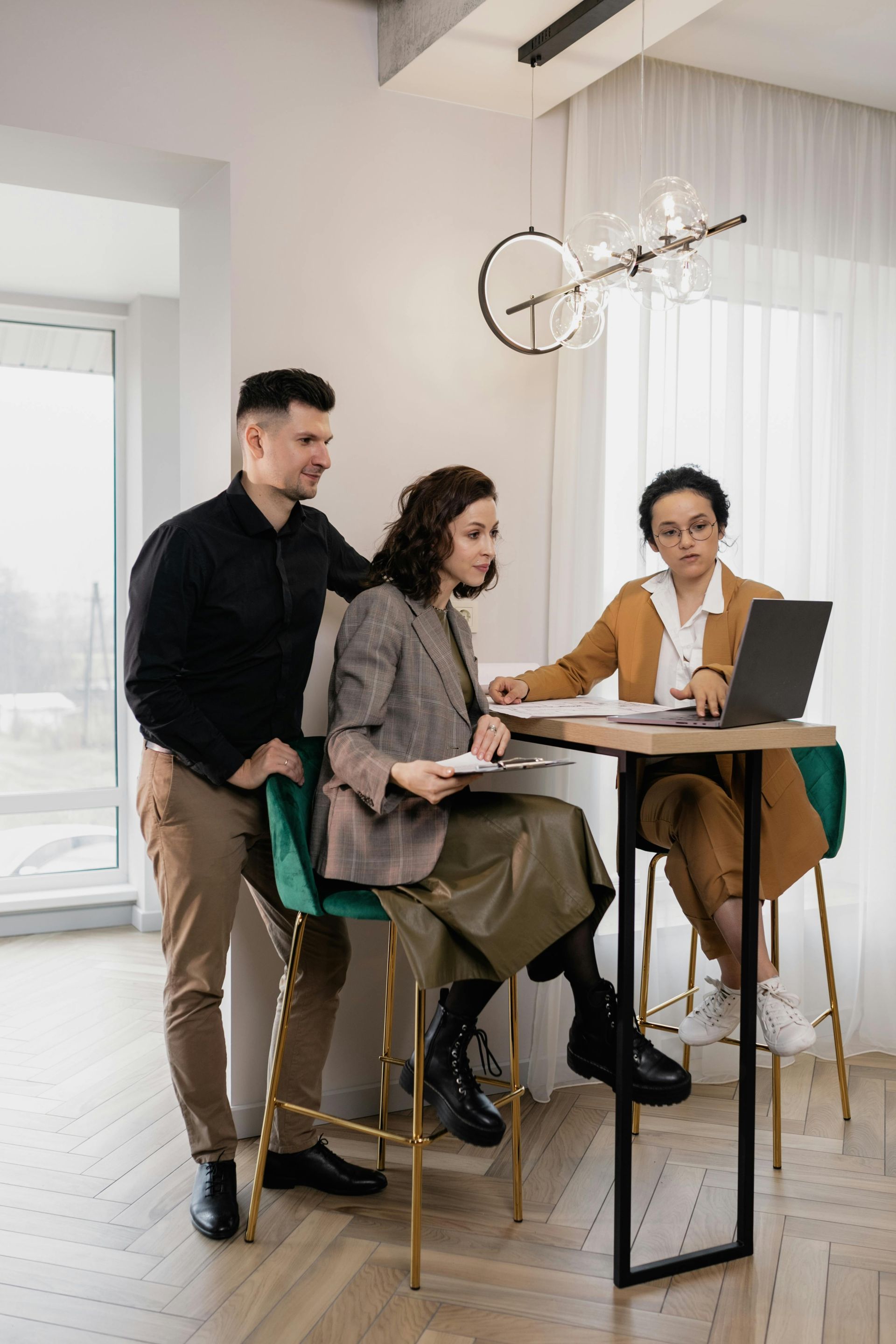 Person in a suit smiles at a couple. They sit at a desk with papers and a laptop in an office.