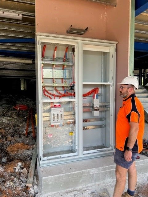 A man in an orange shirt is standing in front of an electrical box