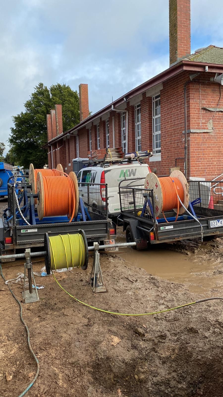 A couple of trailers with hose reels on them are parked in front of a brick building.