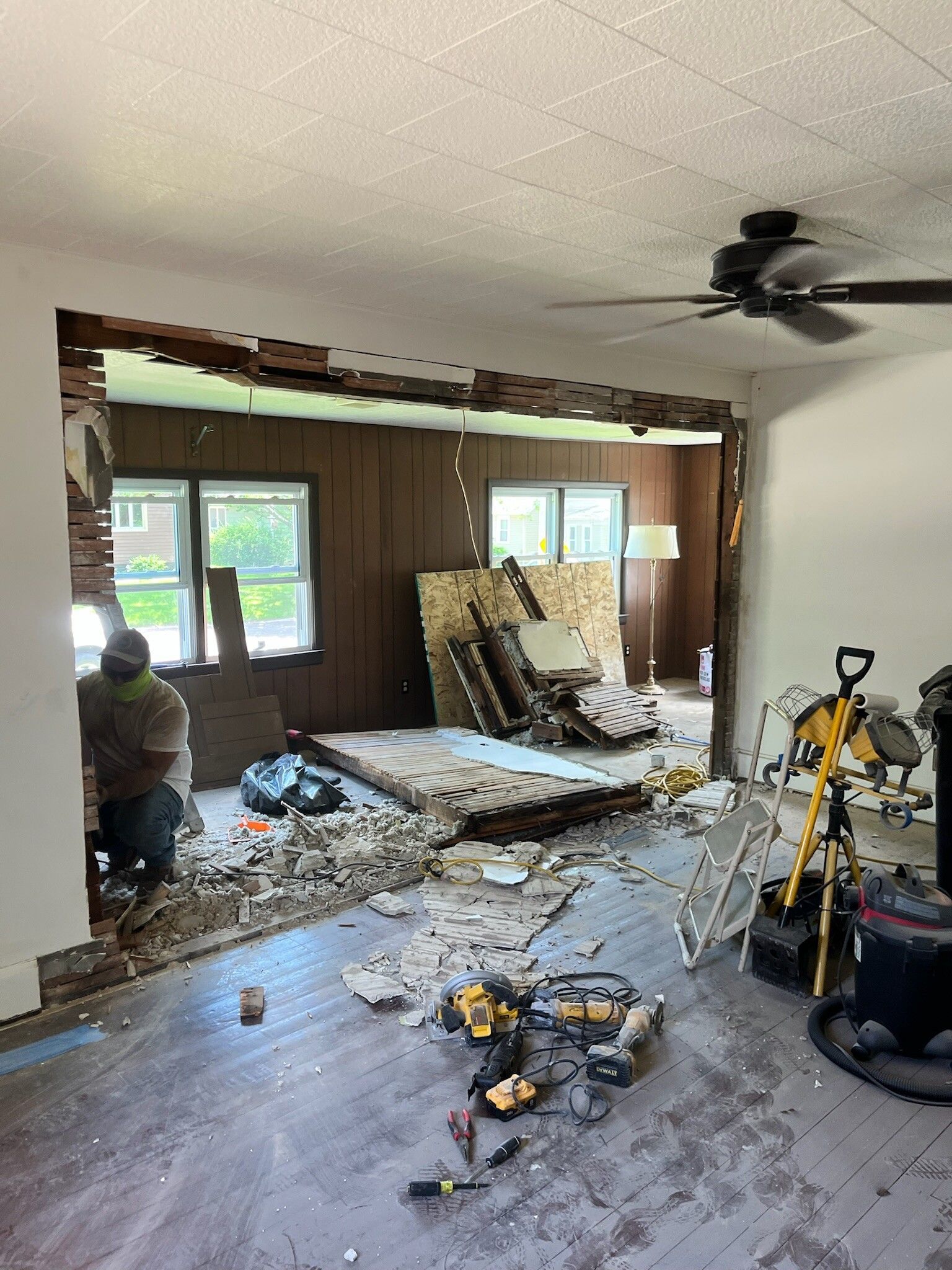 Damaged living room under renovation, with debris, exposed wall, and tools scattered on the floor.