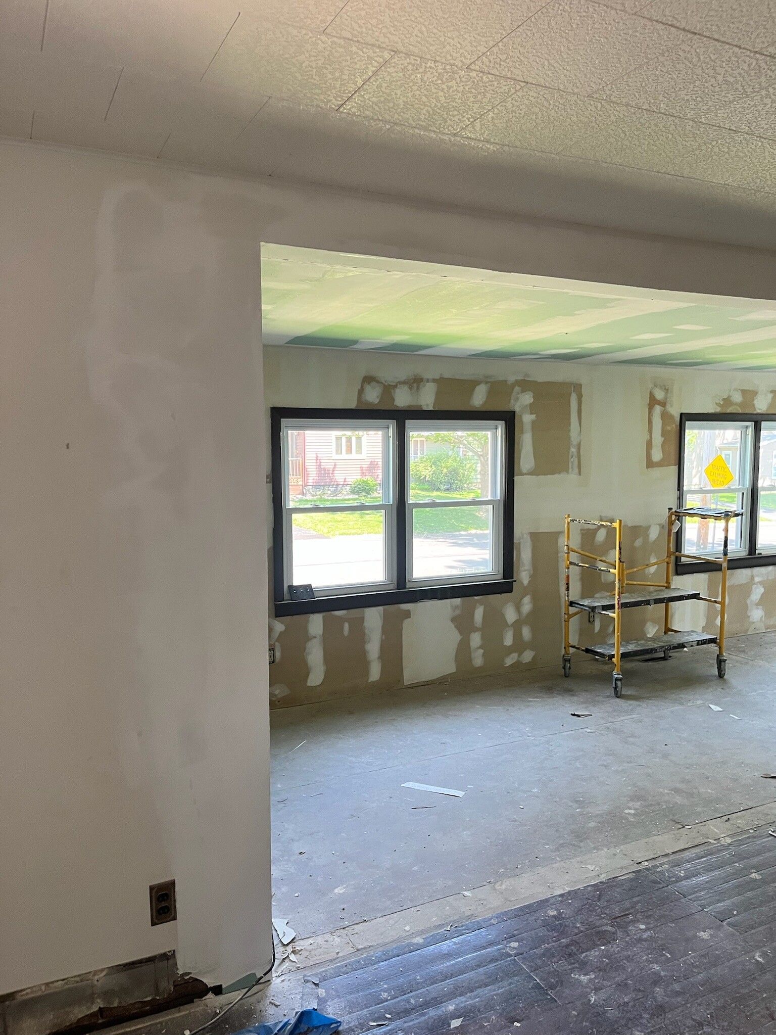 Partially renovated interior room with bare walls, windows, and a ladder under construction debris