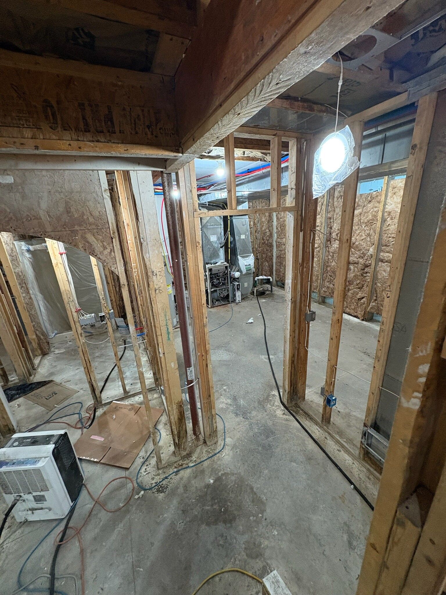 Unfinished basement framing with exposed wood studs, concrete floor, and a bright window opening.