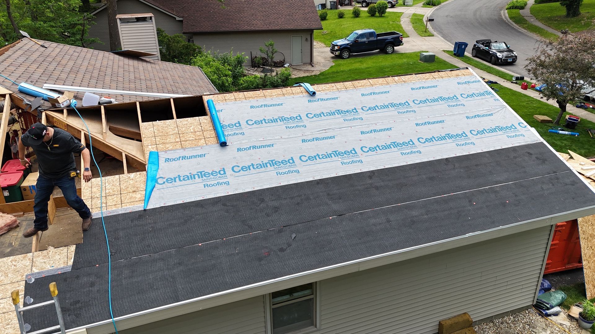Workers replacing a roof, with new underlayment and dark shingles partly installed on a house