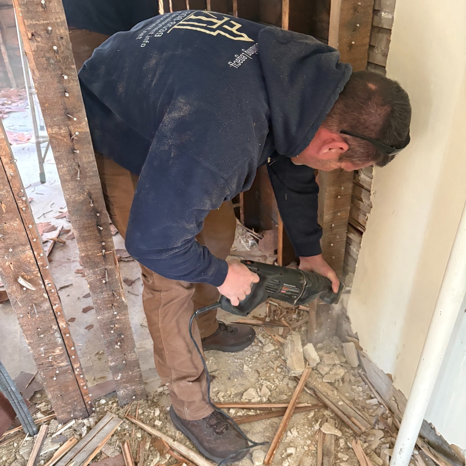 Worker using a power drill to break up debris in a wall opening during home renovation